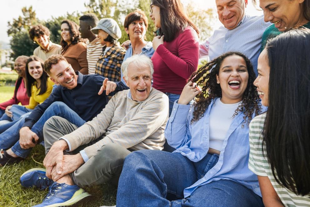 A candid shot of a diverse group of multigenerational people smiling in a line, ready to have a photo taken.